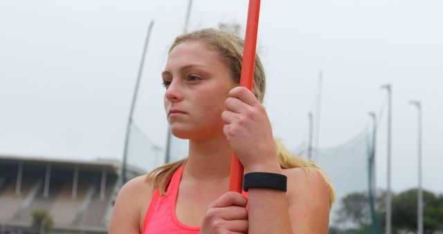 Front view of young Caucasian female athlete standing with javelin stick at sports venue. She is standing at sports venue 4k