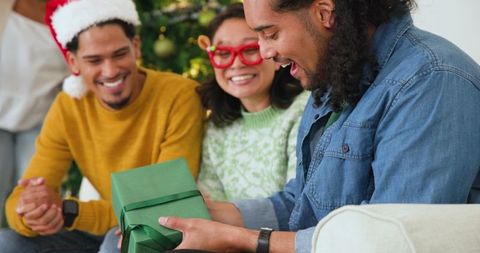 Friends Celebrating Christmas Unwrapping Gift Near Decorative Tree
