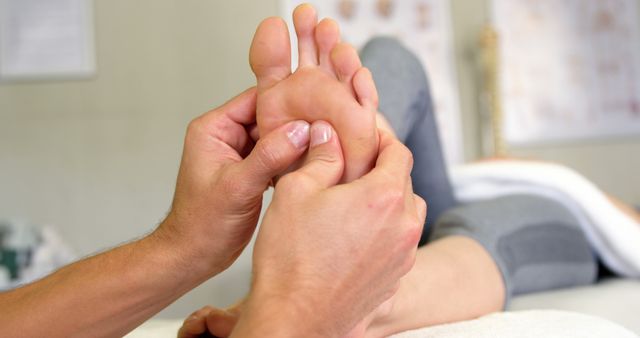 Male massage therapist performing reflexology massage on client's foot in wellness center. Useful for promoting health and wellness services, spa and massage therapy advertisements, or illustrating holistic treatment practices.