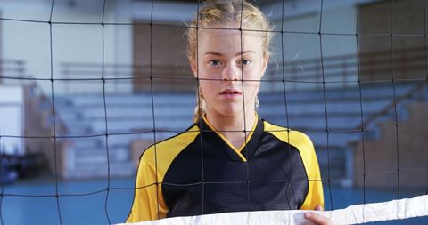 Young female volleyball player holding net in sports arena