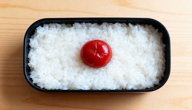 Minimalist japanese bento with umeboshi centering fluffy steamed rice in black box