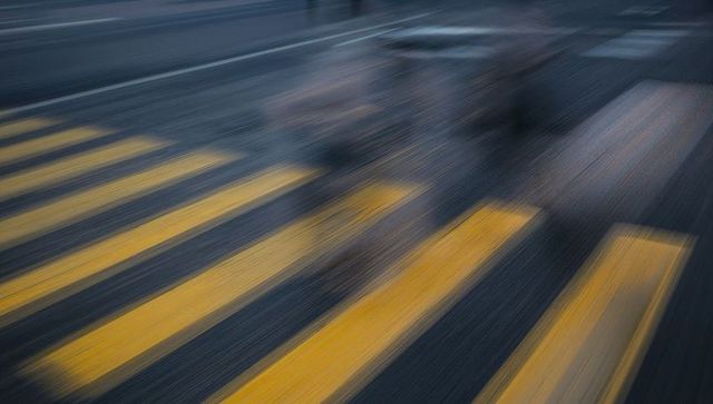 Blurred commuters crossing wet crosswalk at night, glowing zebra stripes and reflections