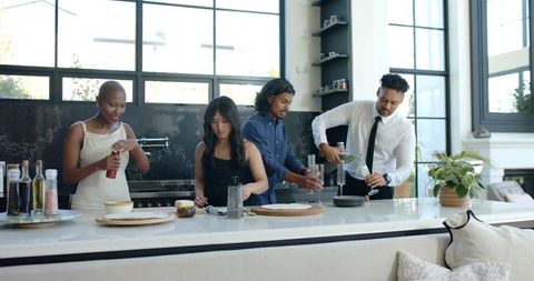 Diverse friends preparing dinner and pouring wine at modern kitchen island