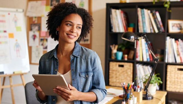 Creative professional holding tablet and smiling while planning in organized home studio