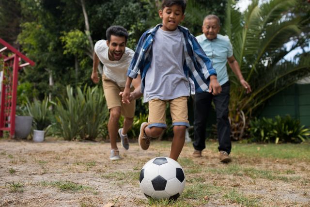 Boy enjoying soccer game with father and grandfather in yard. Perfect for themes of family bonding, outdoor activities, childhood fun, and multigenerational relationships. Ideal for advertisements, family-oriented content, and lifestyle blogs.