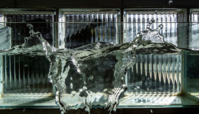 Backlit water splashing refracting light through glass block window on shallow tank sill