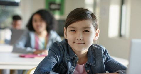 Asian Schoolgirl Smiling in Bright Classroom While Learning on Laptop