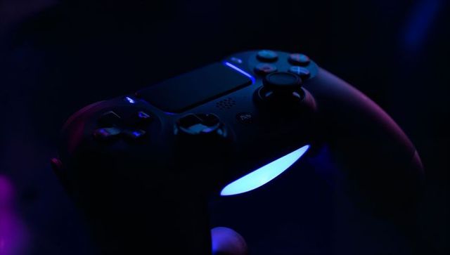 Black wireless gamepad holding with blue-purple led glow for moody neon gaming visual