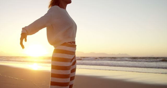A young Caucasian woman enjoys a serene moment on the beach at sunset, with copy space. Her relaxed posture and the warm glow of the sun create a peaceful and reflective atmosphere.
