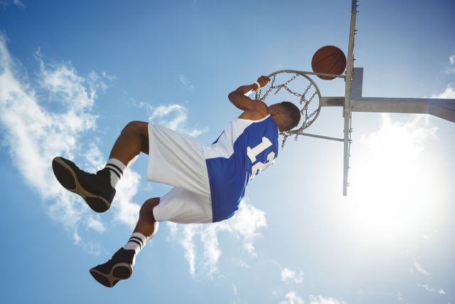 Teenager Hanging on Basketball Hoop Against Blue Sky - Download Free Stock Photos Pikwizard.com