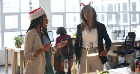 Diverse female coworkers celebrating office holiday with champagne and festive accessories