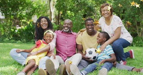 Multigenerational family laughing and relaxing on lawn with soccer ball and golden stars