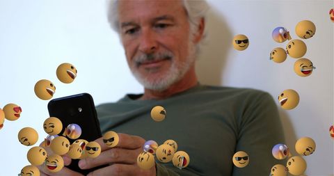 Senior man engaging with digital emojis on smartphone