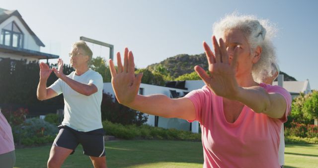 Senior adults performing Tai Chi in a residential garden area. Ideal for content related to elderly fitness, outdoor activities, wellness practices, senior health, and group exercise sessions.