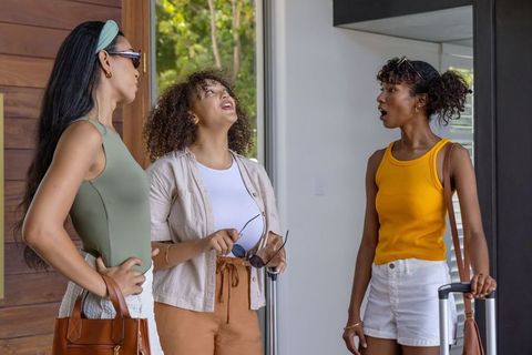 Multiracial women arriving at doorway with suitcases and handbags, expressing surprise