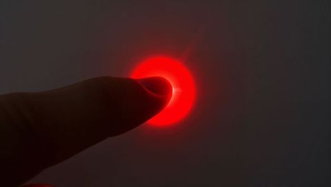 Finger pressing red led button with radiant halo closeup on minimal gray control panel