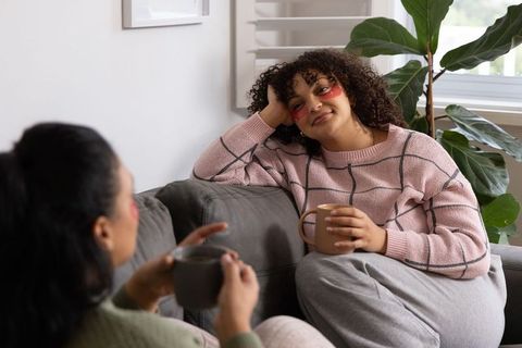 Cozy self-care gathering: diverse women relaxing with under-eye patches and mugs on couch