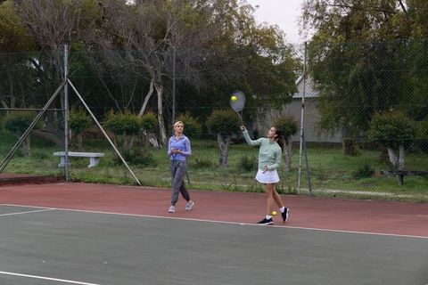 Female friends playing tennis on outdoor park court practicing serves and rallying together