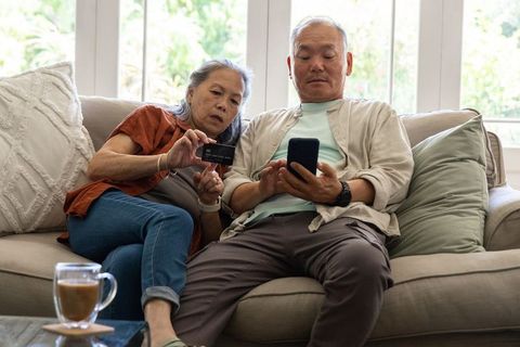 Senior asian couple using smartphone and credit card for online transactions at home