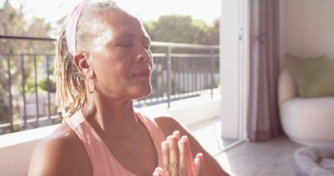 Senior woman meditating on sunny balcony for peaceful relaxation