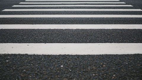 Receding pedestrian crosswalk with bold white stripes on textured asphalt leading lines