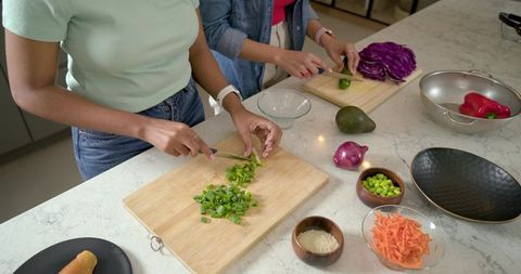 Diverse women chopping and slicing colorful vegetables on kitchen counter preparing salad