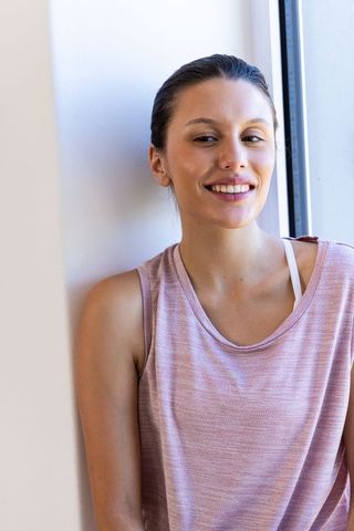 Smiling african-american woman leaning by window in pink knit top, natural light portrait