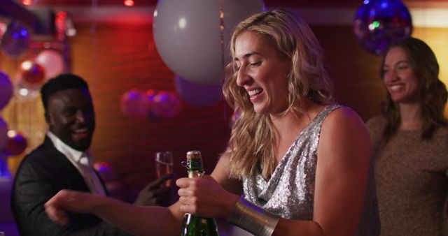 Image of happy caucasian woman uncorking bottle of champagne for diverse friends at nightclub. Fun, drinking, going out, inclusivity and party concept.