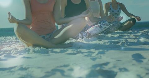 Group beach meditation practicing mindfulness and yoga on sunlit sand by ocean horizon at sunrise