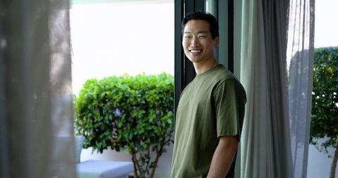 Smiling asian man enjoying morning on sunny patio wearing olive green tee