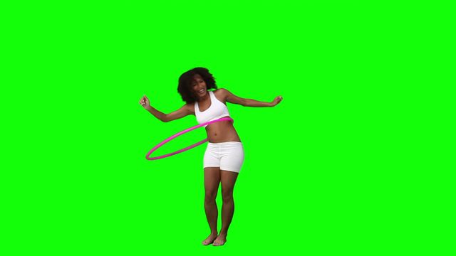 A woman is actively having fun with a hula hoop against a vibrant green screen background, ideal for fitness and wellness promotions. Use for content about joyful activities, healthy lifestyle initiatives, or creative video editing projects requiring a greenscreen.