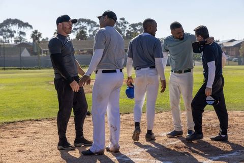 Baseball team gathering on diamond for coach briefing, teammates consoling catcher