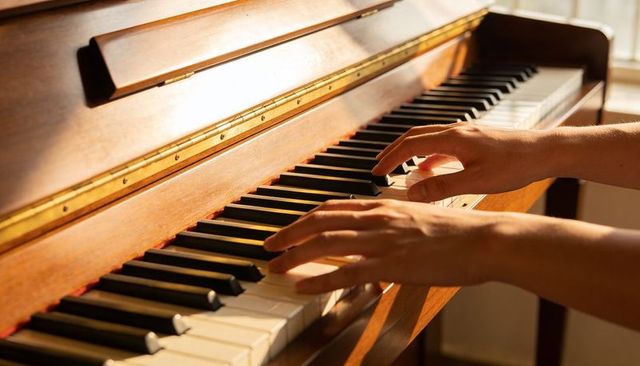 Sunlit hands playing upright wooden piano closeup with brass trim
