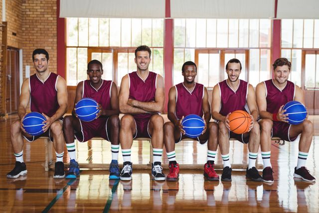 Portrait of smiling basketball players sitting on bench with basketball in the court