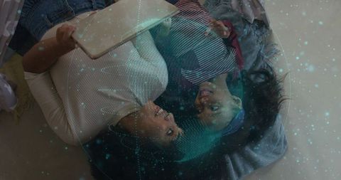 Parent and child lying together using tablet with teal holographic globe overlay