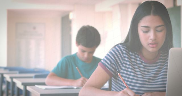 Teen students are diligently studying and taking notes in a classroom environment. The photo features a boy and a girl, both focused on their work. It can be used for educational websites, school brochures, or advertisements focusing on academic achievement and learning environments.