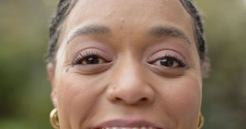 Close-up smiling woman with braided hair, nose stud and gold hoop earrings, natural gaze