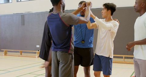 Diverse male basketball players giving team high five during indoor training huddle on court