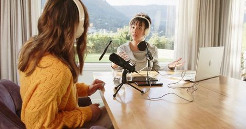 Two women recording podcast at home with laptop, condenser microphone and headphones