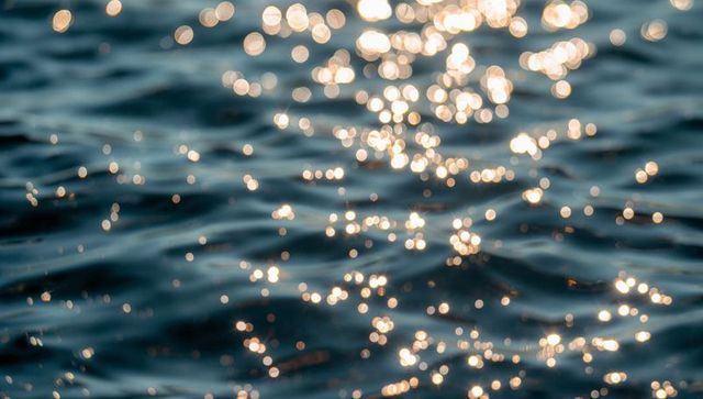 Sunlit ocean ripples creating golden bokeh on deep blue-green water