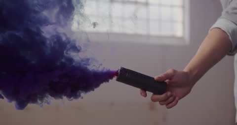 A young person holding a colored smoke container in an industrial space releases a plume of vibrant purple smoke. This dynamic scene conveys themes of creativity and bold expression, suitable for use in advertising for artistic events, urban culture promotions, or inspirational content highlighting individuality and self-expression.