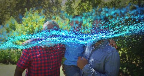Family holding child and embracing while cyan particle light trail swirling in sunny park