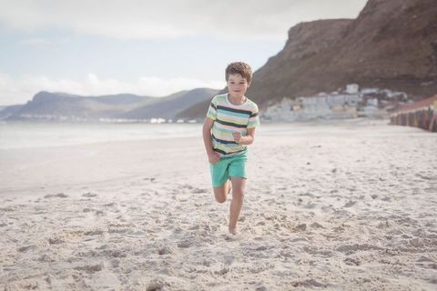 Joyful Boy Running Free on Sandy Beach Near Vibrant Huts