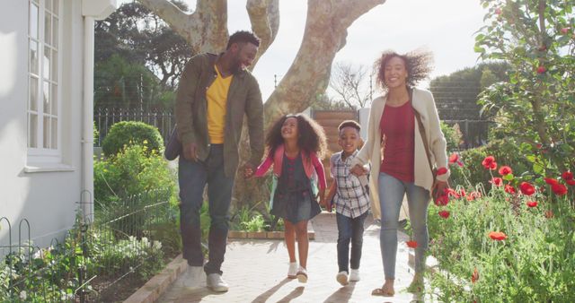 Happy African American family walking in a beautifully landscaped garden with children holding hands. Perfect for use in advertisements, promotional material for family-oriented products, websites about parenting and family activities, or social media content celebrating togetherness and outdoor lifestyle.