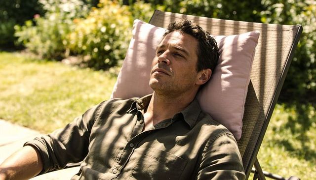 Contemplative man reclining on patio lounge chair soaking up dappled sunlight in garden