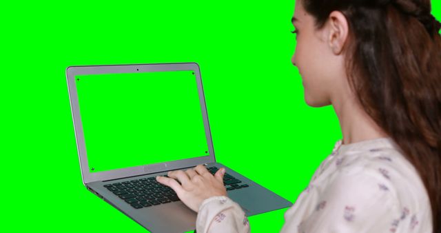 Young woman using a laptop with a green screen, implying flexibility for added digital content. Ideal for presentations, advertisements, tech tutorials, and promotional videos with inserted custom content on the green screen.