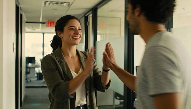 Young colleagues celebrating success with high-five in modern glass office corridor