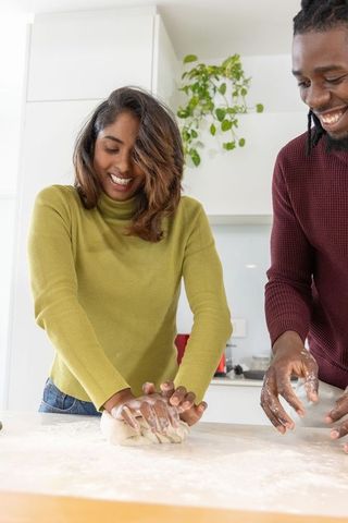 Multicultural couple kneading bread together in bright modern kitchen, sharing joy