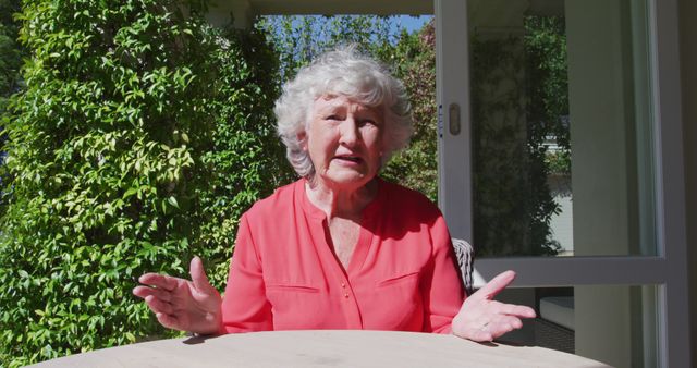 Caucasian senior woman sitting at table in sunny garden talking and gesturing. at home in isolation during quarantine lockdown.