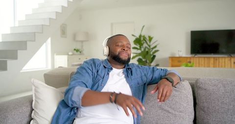 African american man relaxing on couch listening to music with wireless headphones